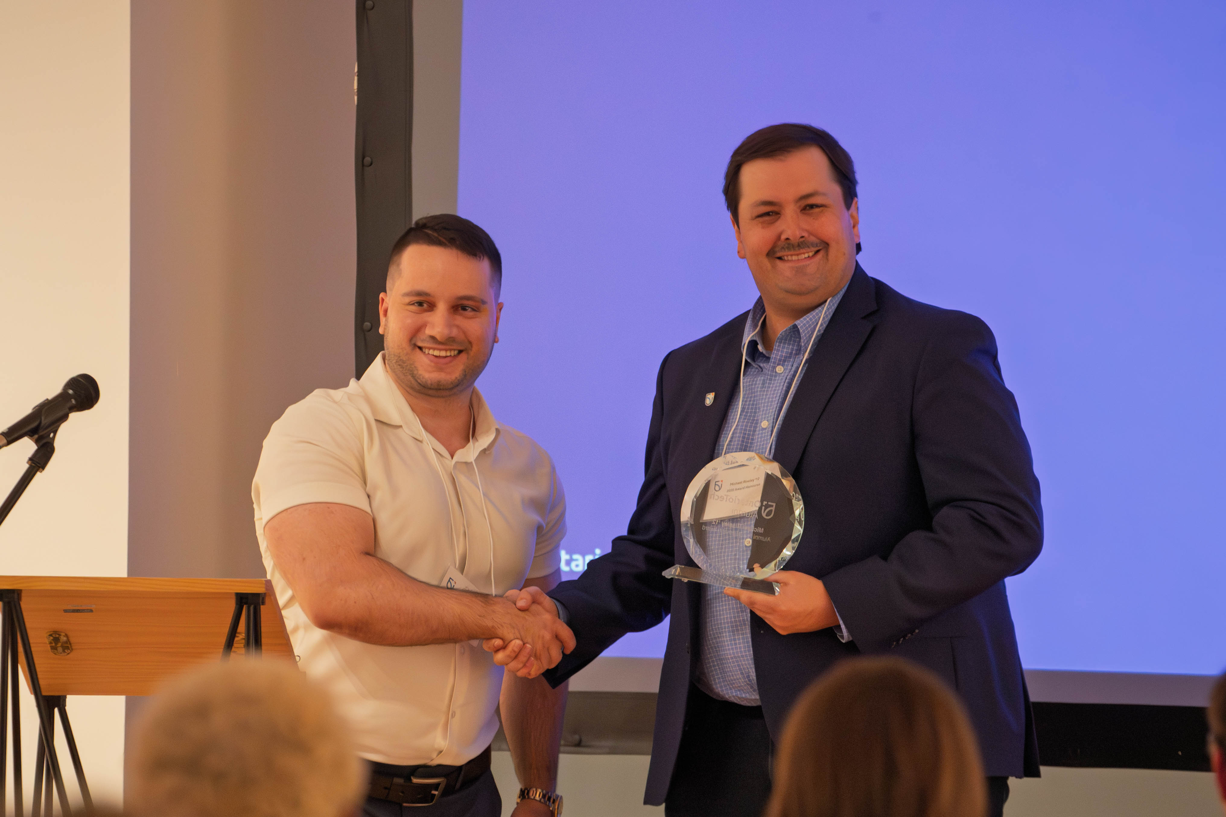Two men shaking hands, one is holding award